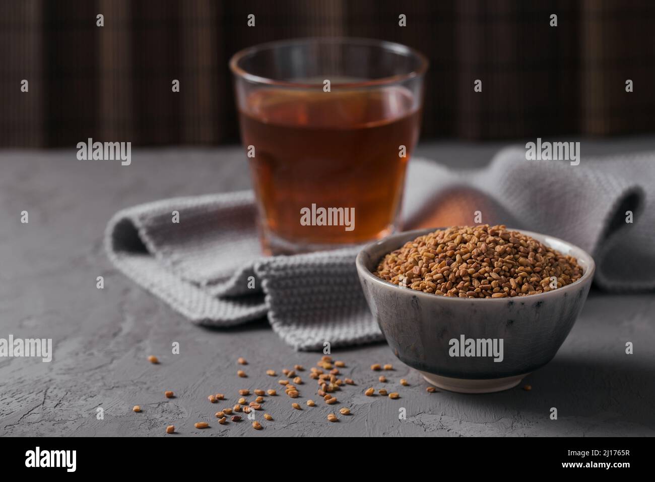 Bowl of fenugreek seeds and Egyptian fenugreek yellow tea or Methi Dana drink on grey background Stock Photo