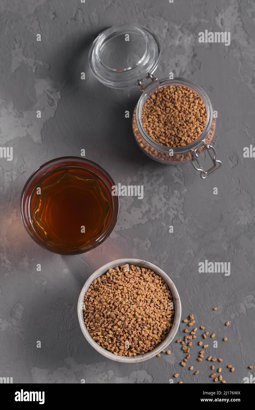 Glass of Egyptian fenugreek yellow tea, Helba or Methi Dana drink and fenugreek seeds on grey background Stock Photo