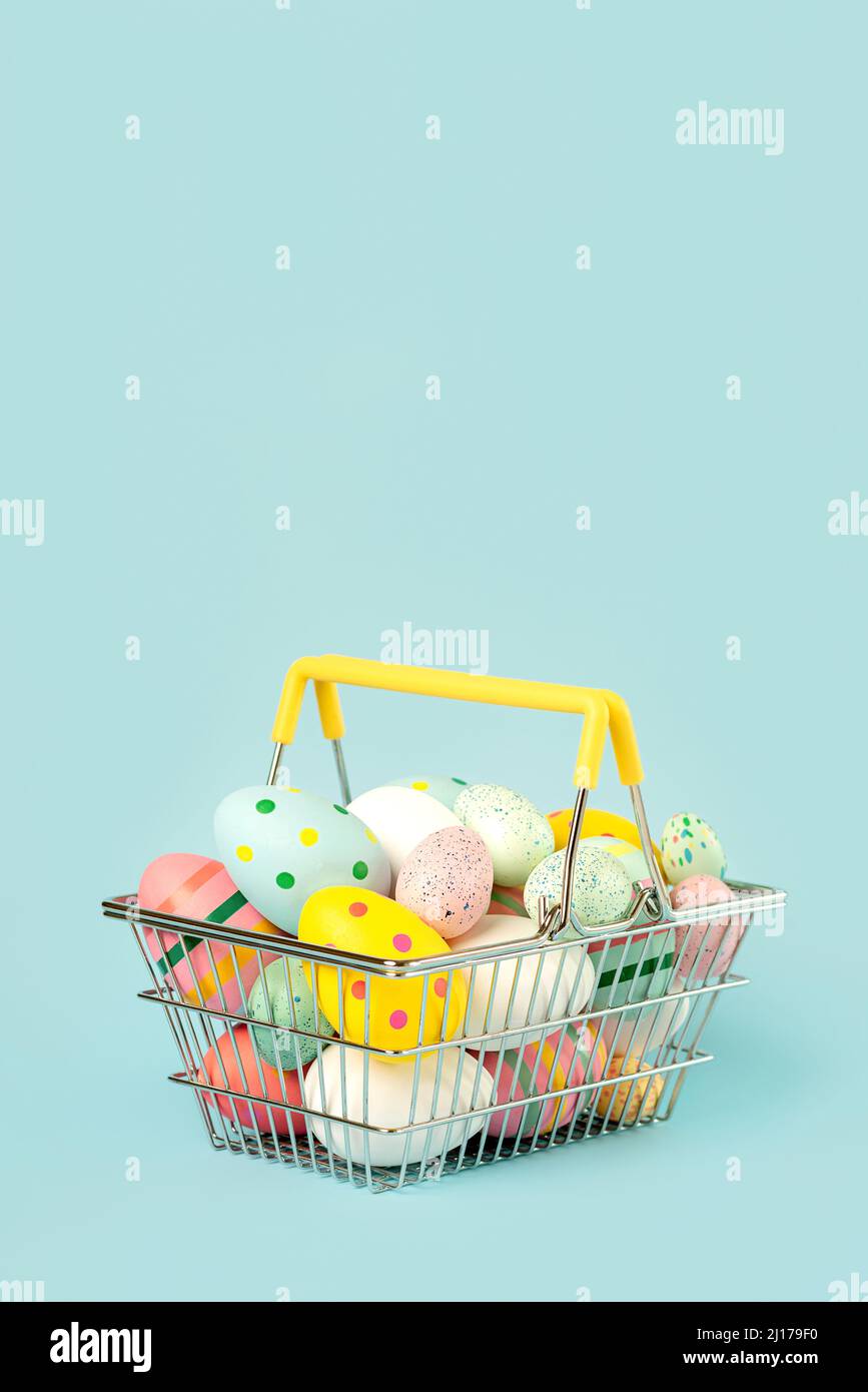 Happy Easter. Colored easter painted eggs in a shopping basket with copy space over blue background Stock Photo