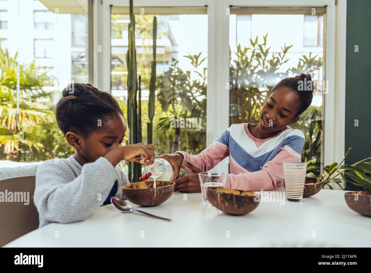 Girl pouring milk in bowl for sister at dining room Stock Photo