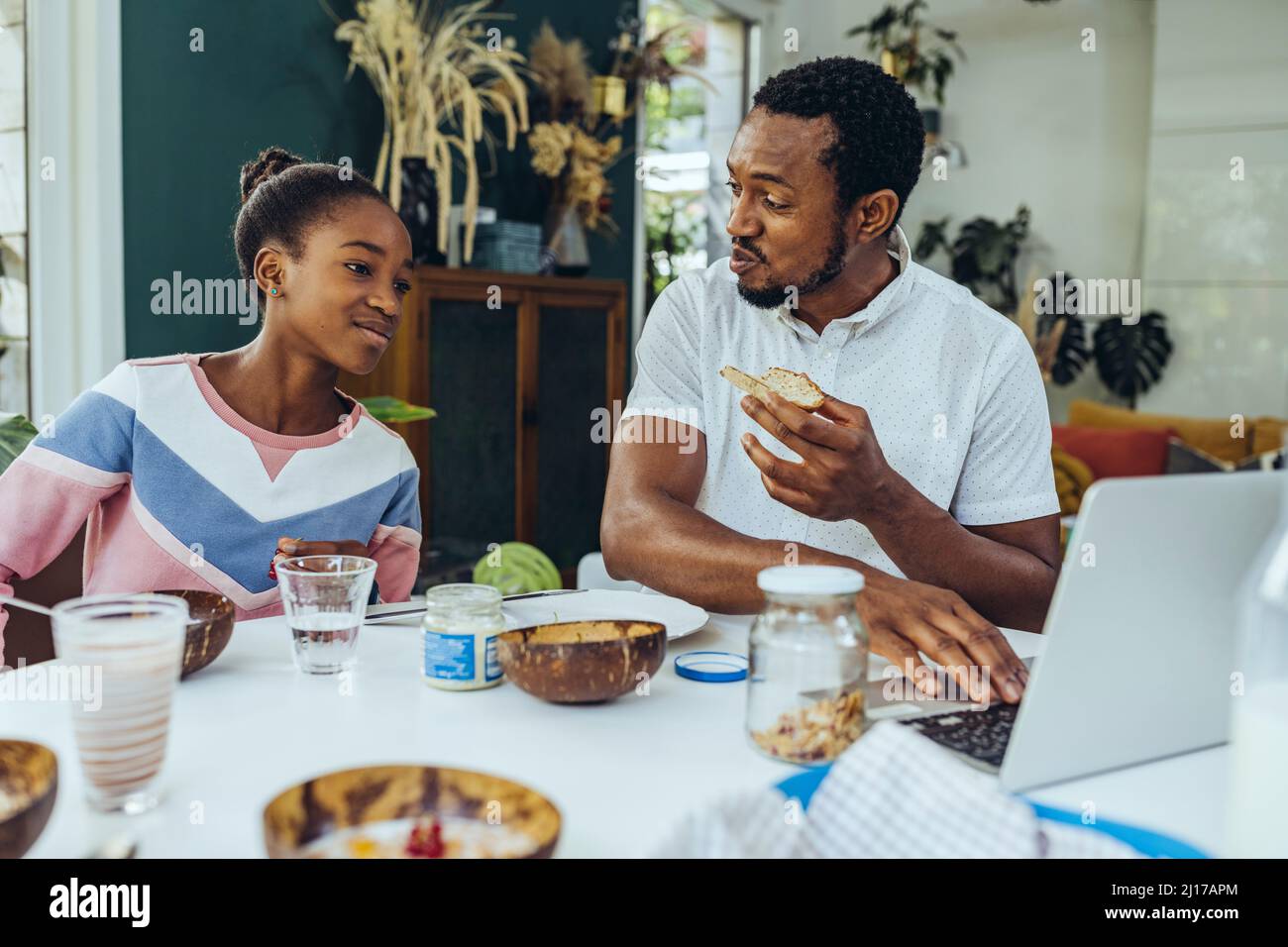 Father and daughter using a laptop at breakfast table Stock Photo