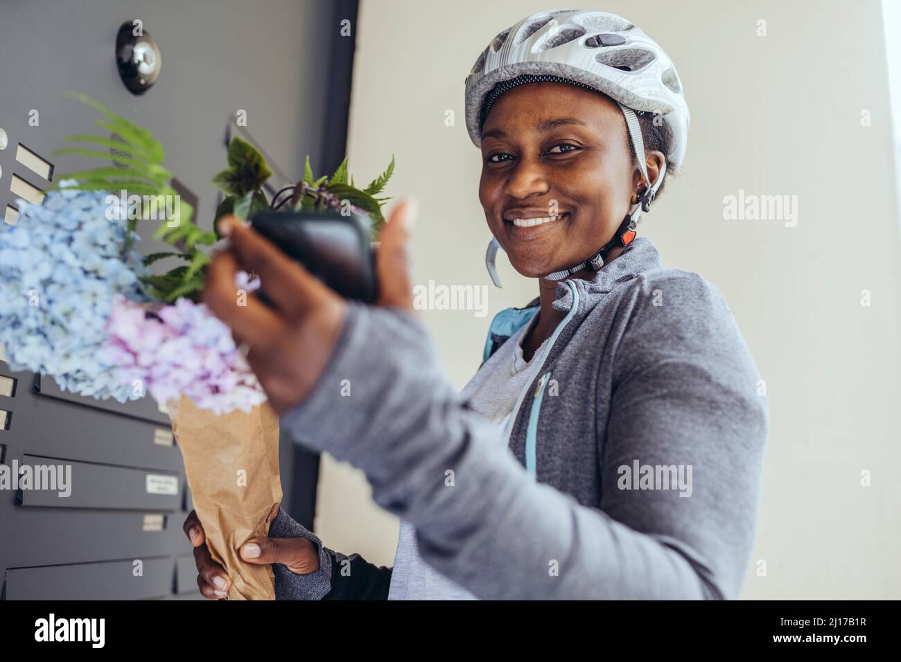 Smiling delivery woman with bouquet at entrance door Stock Photo
