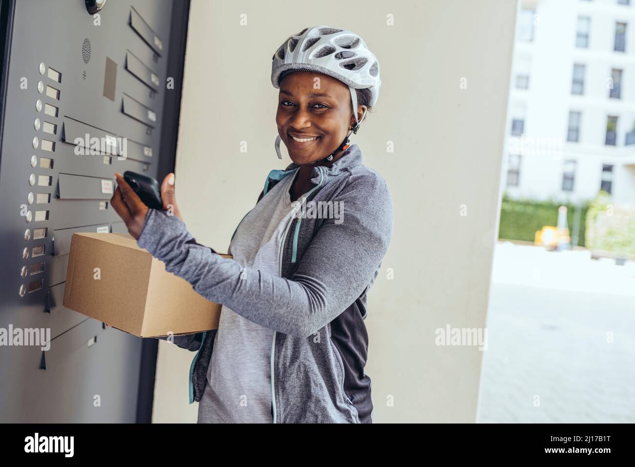 Smiling delivery woman with package box at entrance door Stock Photo