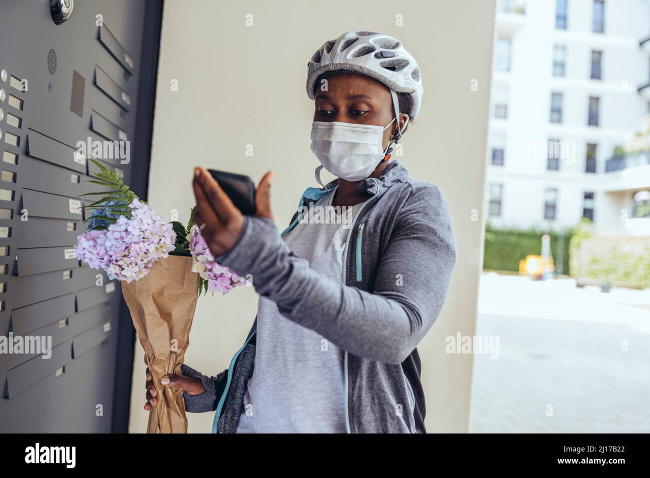 Delivery woman with protective face mask holding bouquet at entrance door Stock Photo