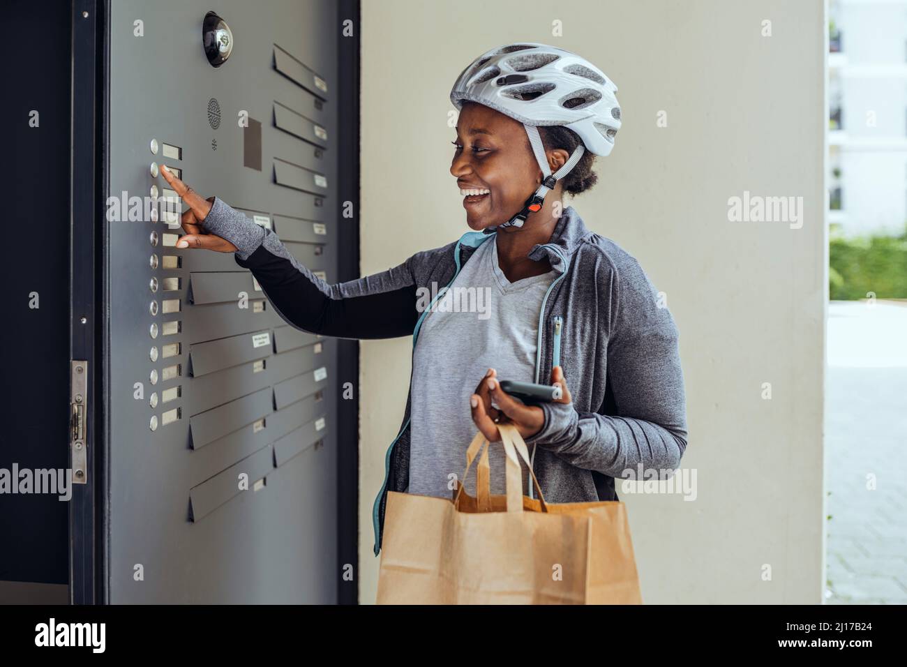 Happy delivery woman pushing button at entrance door Stock Photo