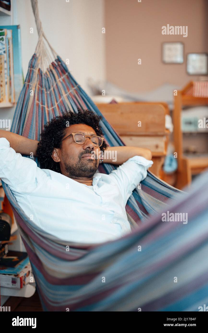 Man with hands behind head resting in hammock at home Stock Photo