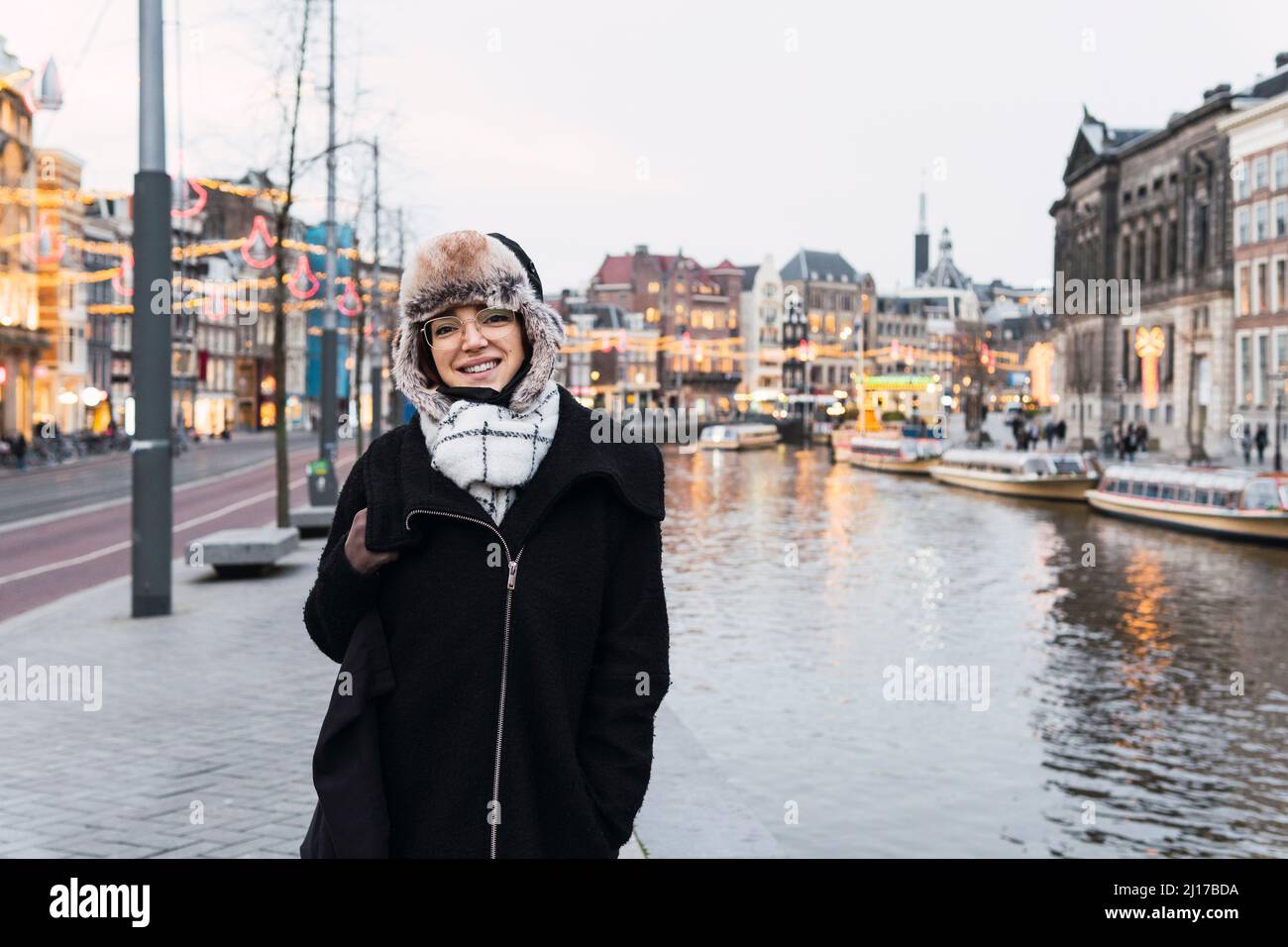 Smiling woman in winter hat by canal in city Stock Photo