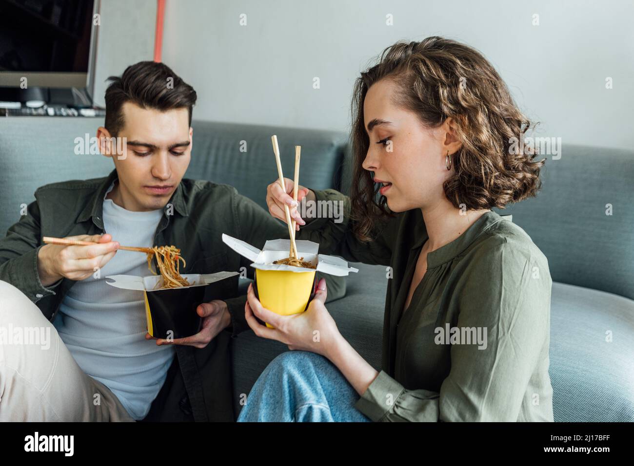 Young couple with chopsticks eating noodles at home Stock Photo