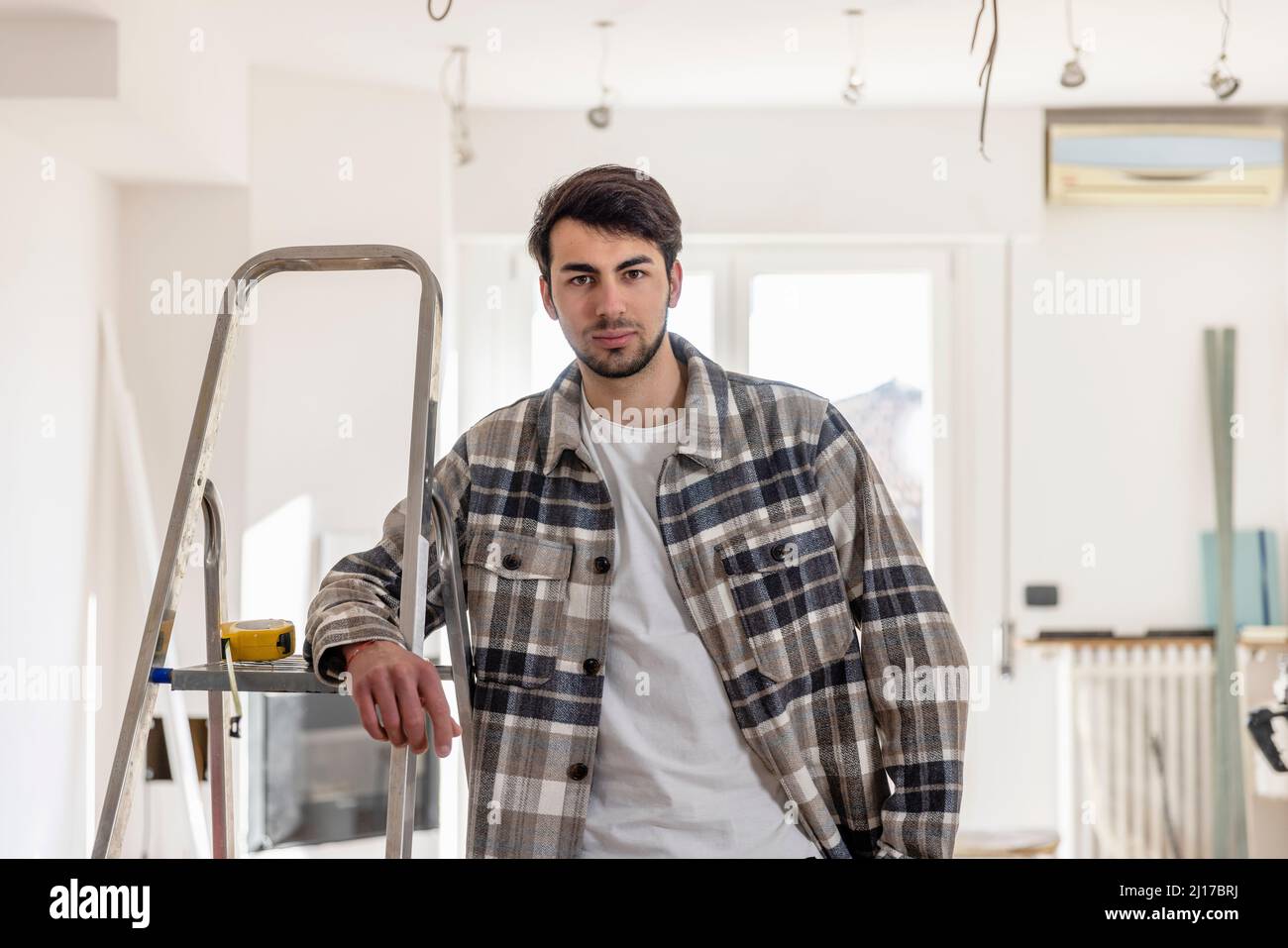 Young man standing by ladder at home Stock Photo