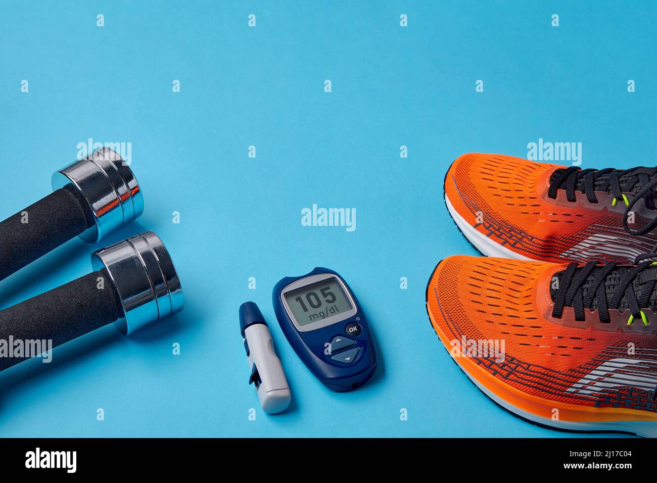 Orange sneakers, metal dumbbells and a blood glucose meter on a blue background. Exercise to overcome insulin resistance Stock Photo
