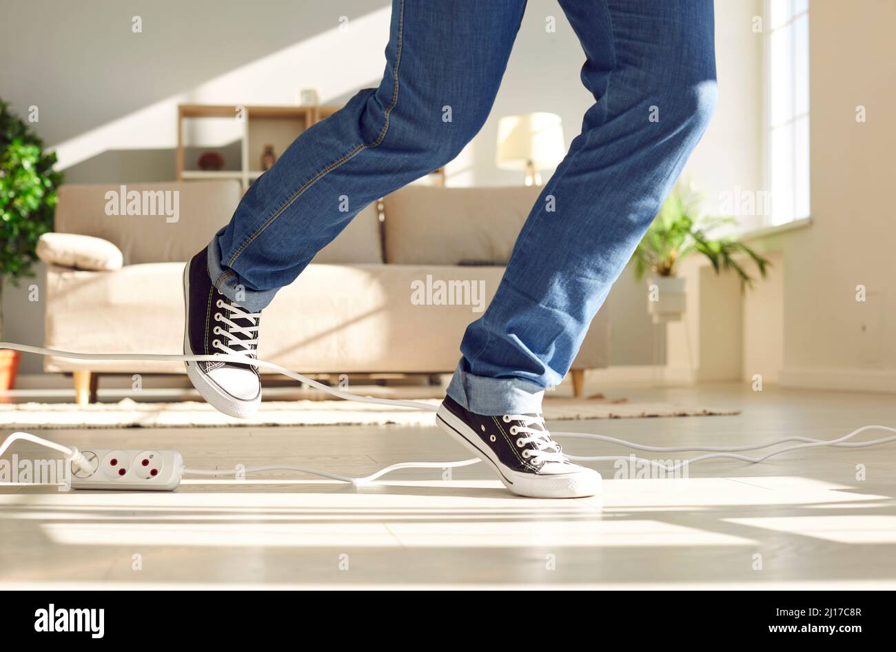 Young man tripping over a power cable at home, close up shot of his feet on the floor Stock Photo
