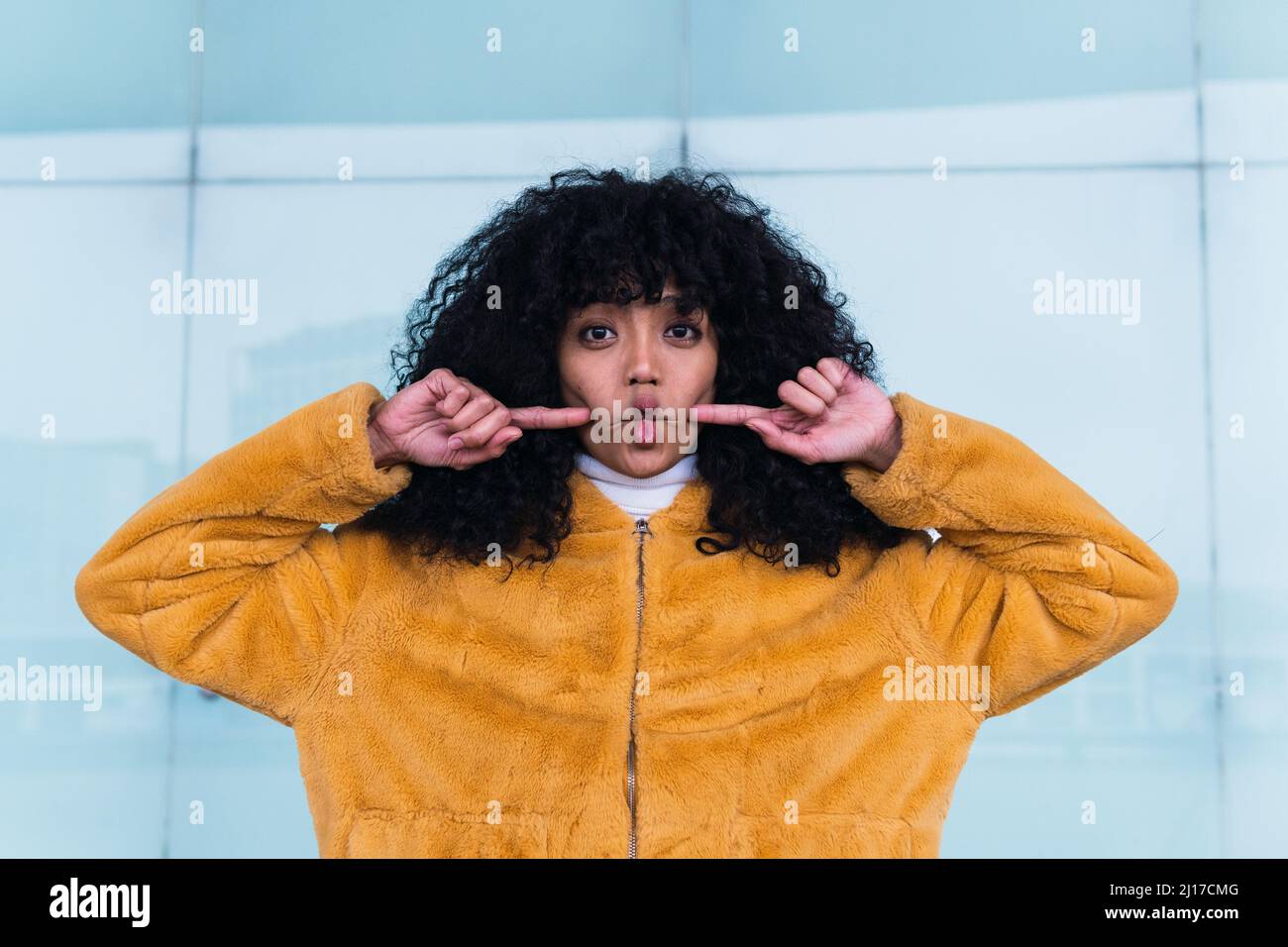 Young woman making fish face grimace in front of wall Stock Photo