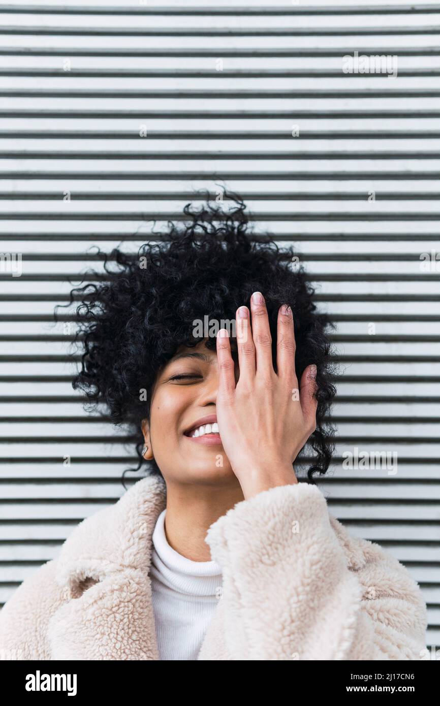 Smiling young woman covering face in front of wall Stock Photo - Alamy
