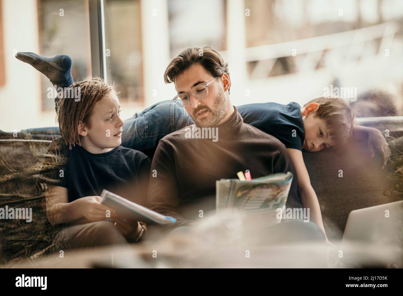 Man explaining to son with boy lying on sofa at home Stock Photo