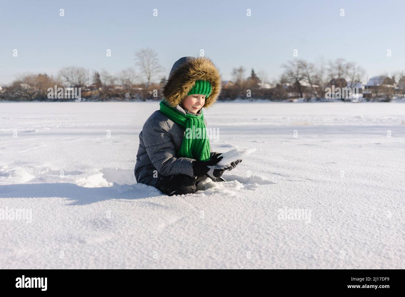 Boy with warm clothing sitting in snow Stock Photo