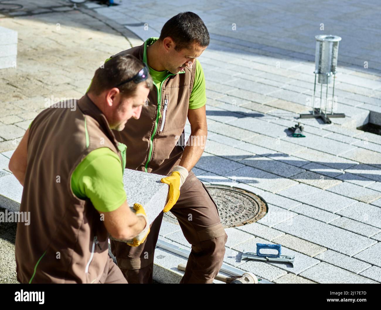 Blue-collar workers carrying paving stone for installing on sidewalk Stock Photo