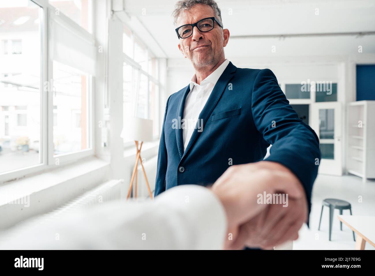 Smiling businessman shaking hand with colleague in office Stock Photo