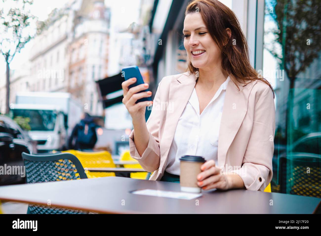 Smiling woman with disposable coffee cup using smart phone in cafe Stock Photo