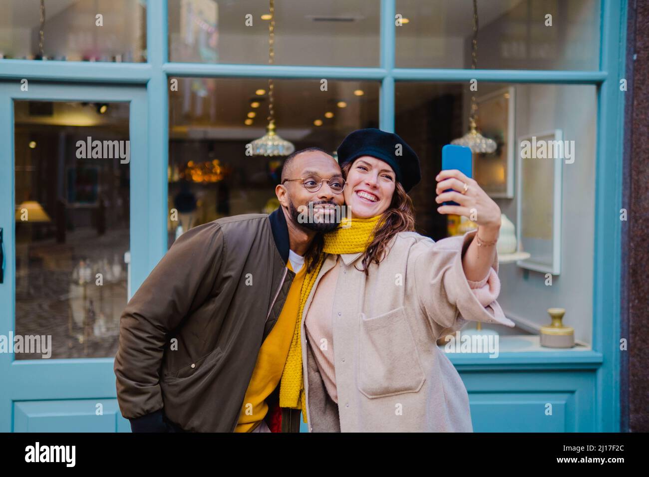 Smiling couple taking selfie on smart phone outside cafe Stock Photo