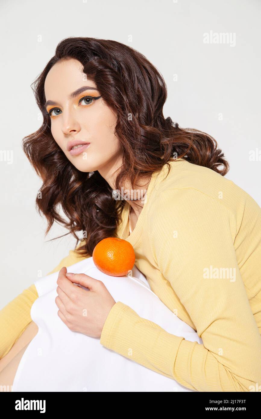 Young woman balancing tangerine on knee at studio Stock Photo