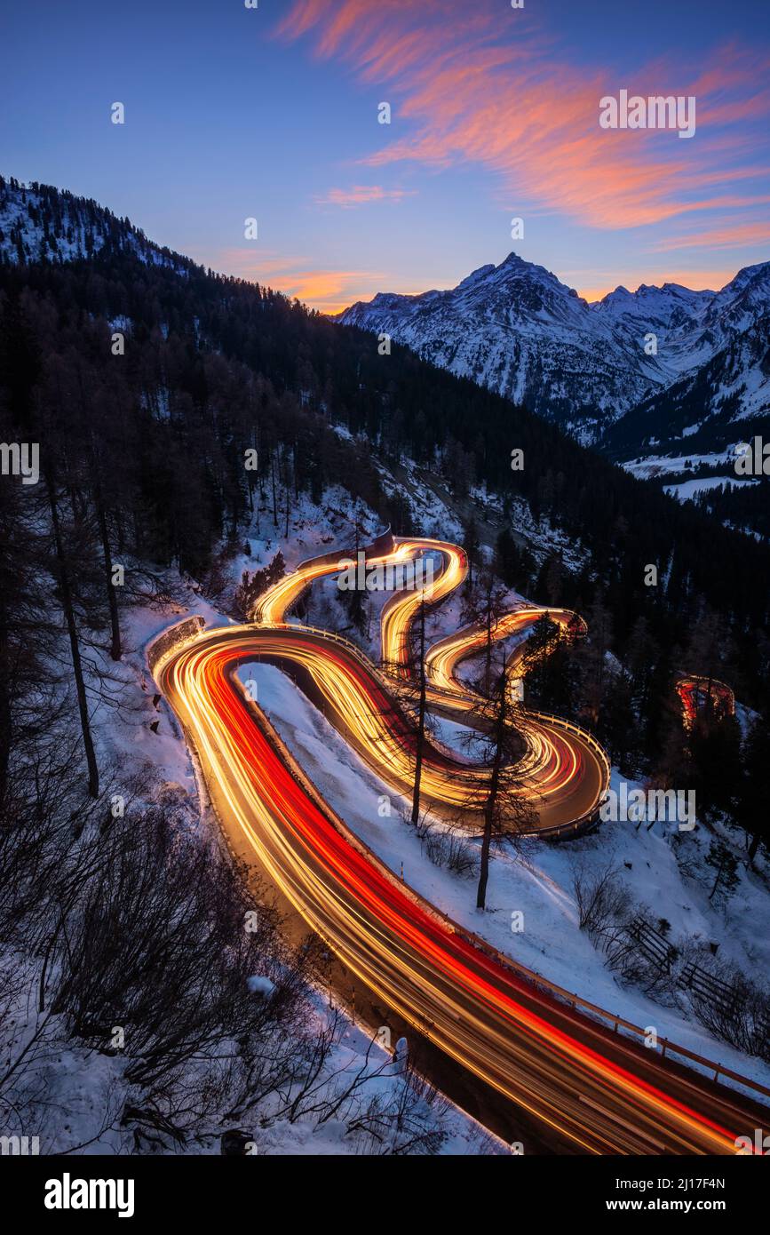 Car light trails stretching along winding road of Maloja Pass at dusk Stock Photo