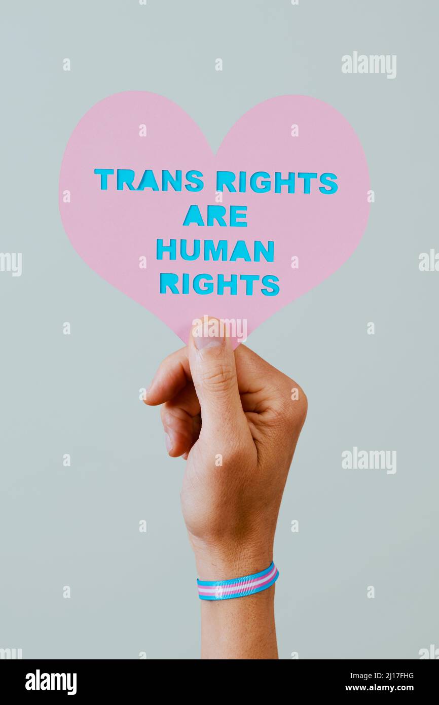 closeup of a young person, wearing a wristband patterned with the transgender pride flag, holding a pink heart with the text transgender rights are hu Stock Photo