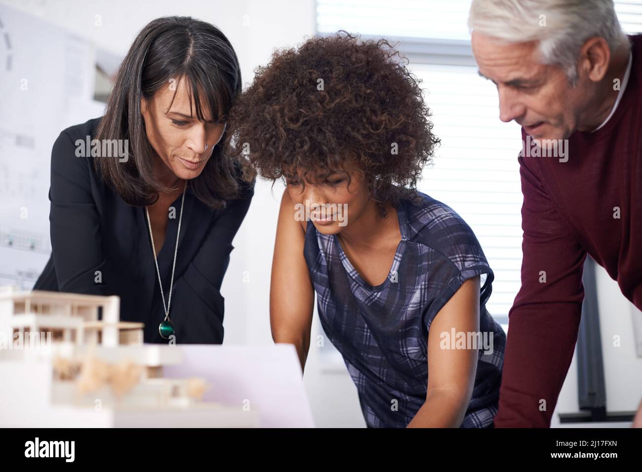 Touching up our prototype. Shot of three architects discussing an architectural model in the workplace. Stock Photo