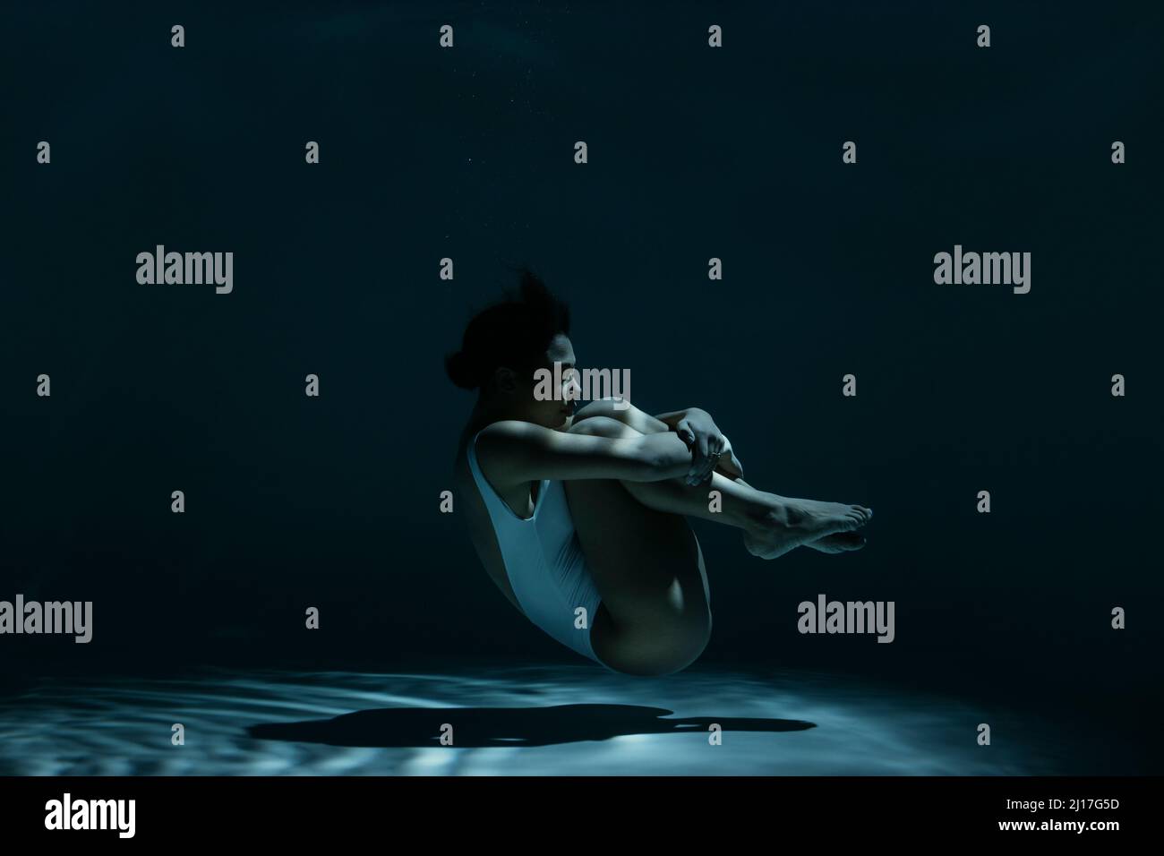 Woman in fetal position swimming underwater Stock Photo