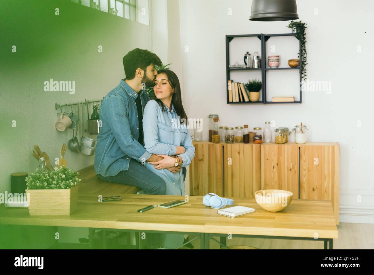 Man kissing on girlfriend's forehead in kitchen Stock Photo