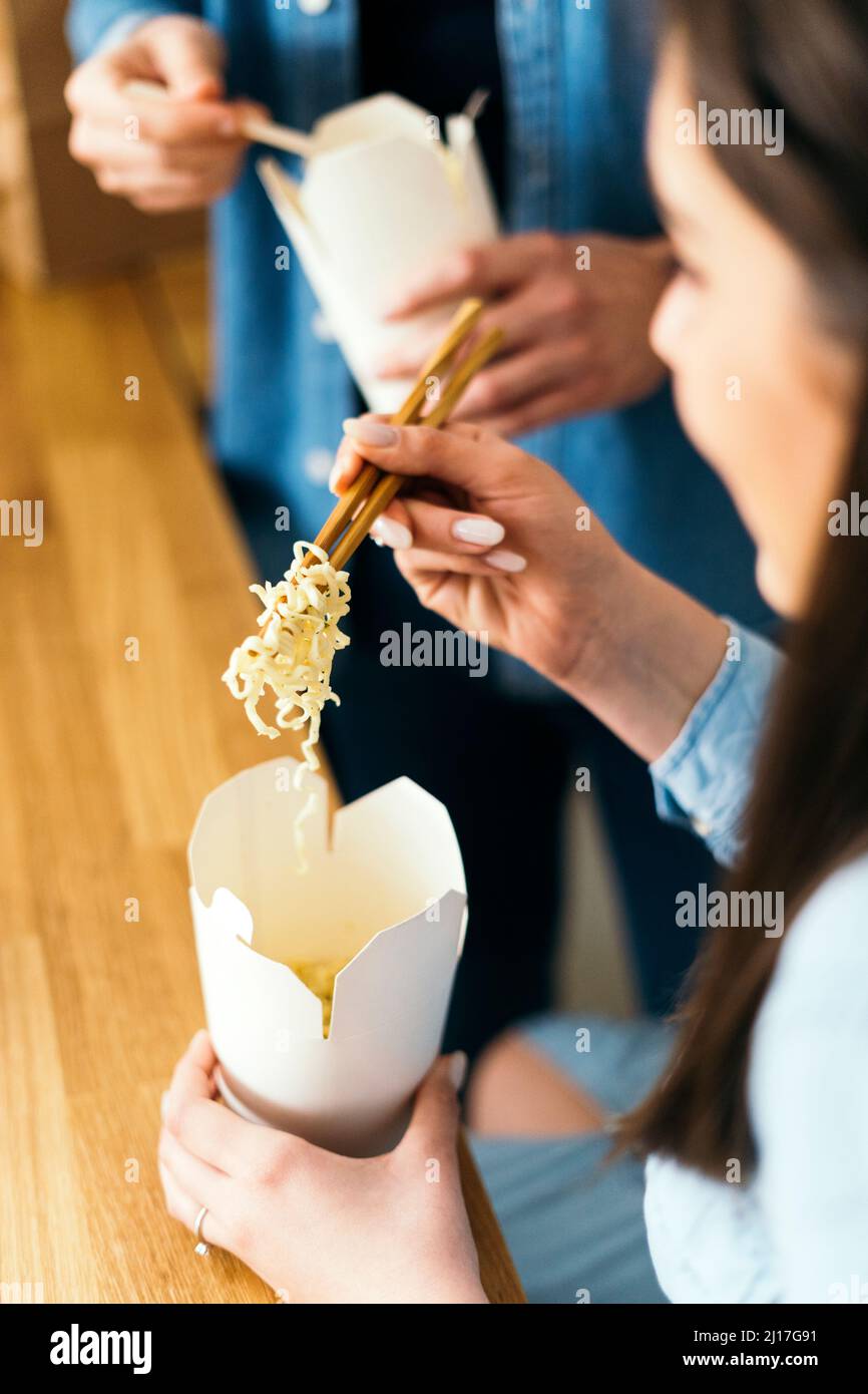 Woman eating noodles with chopsticks in kitchen Stock Photo