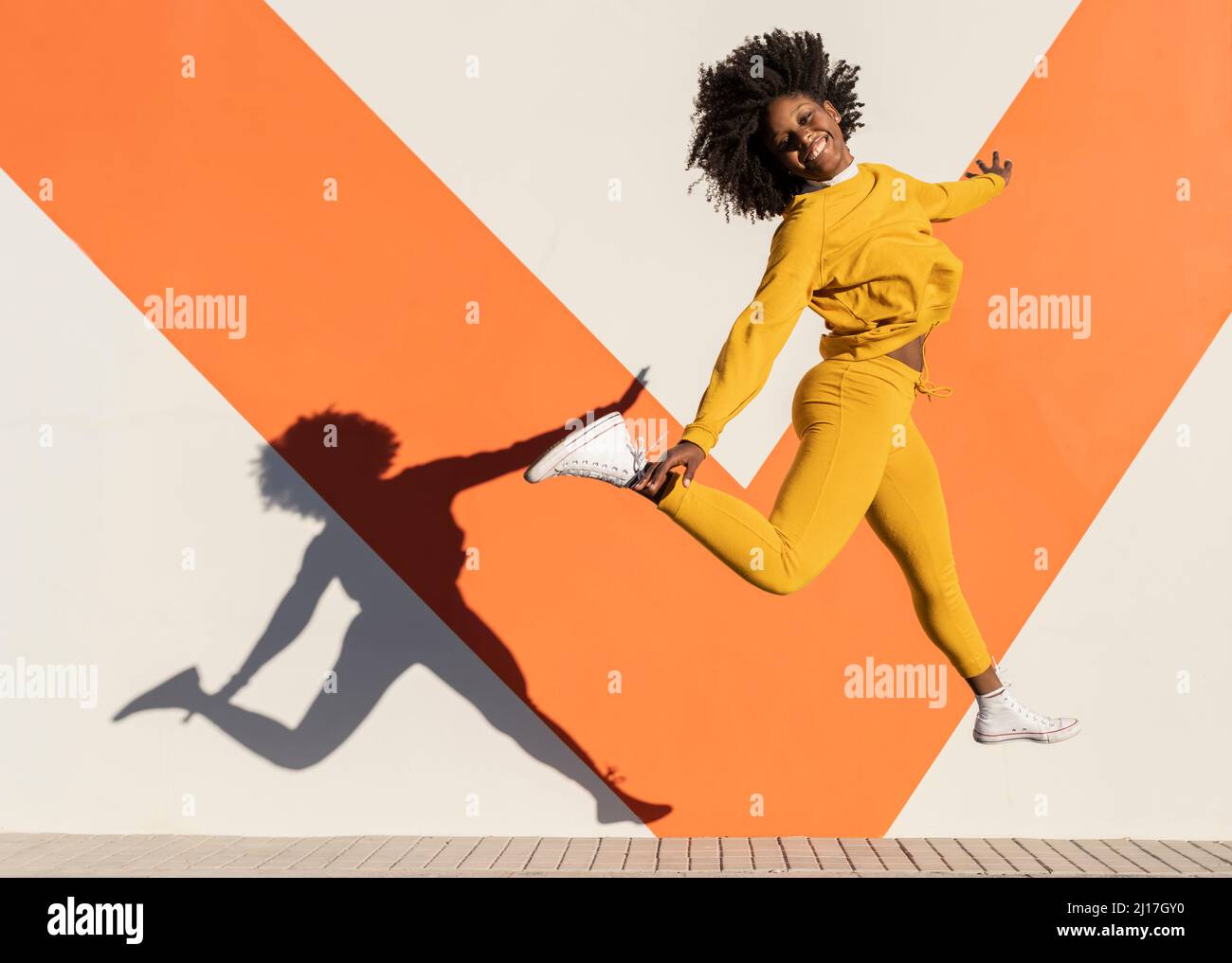 Happy woman jumping by wall on sunny day Stock Photo