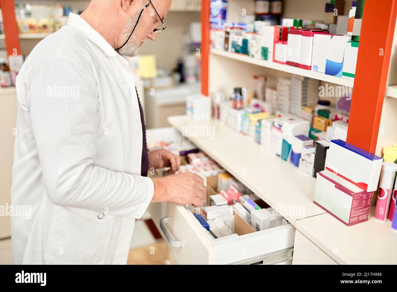 Pharmacist wearing eyeglasses opening drawer of medicines at pharmacy store Stock Photo