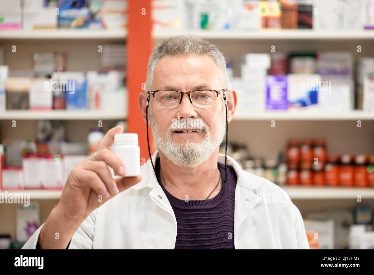 Pharmacist wearing eyeglasses holding bottle of medicine at pharmacy store Stock Photo