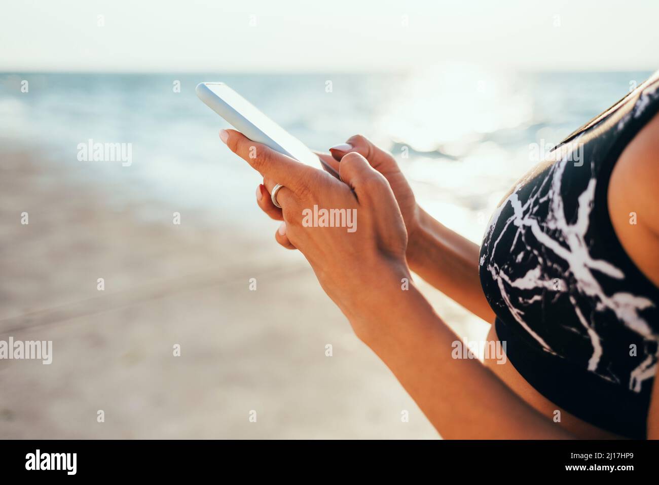 Woman in sports bra using smart phone at beach Stock Photo
