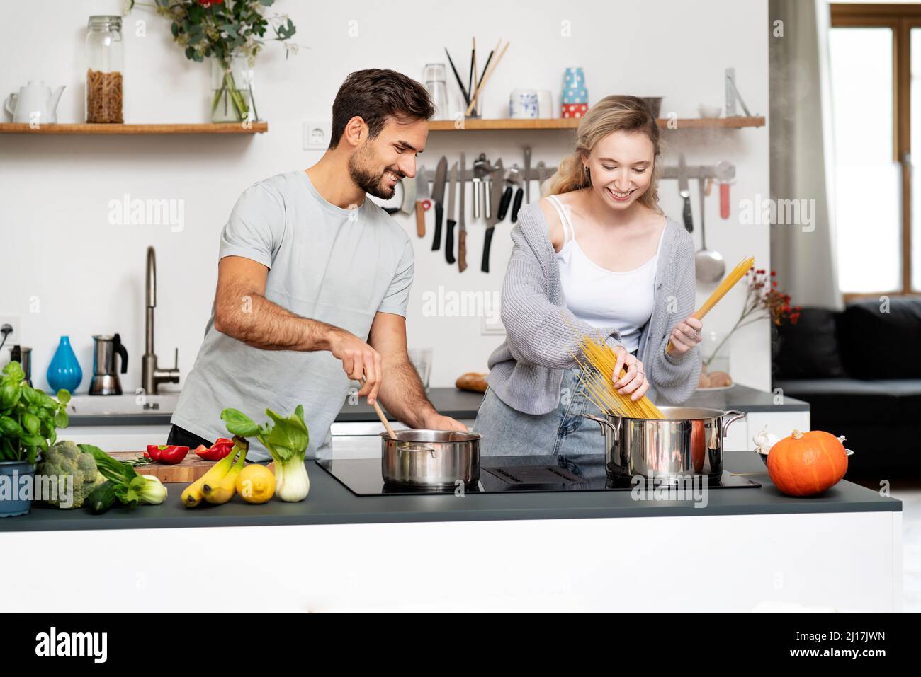 Smiling young man looking at girlfriend making pasta in kitchen Stock Photo