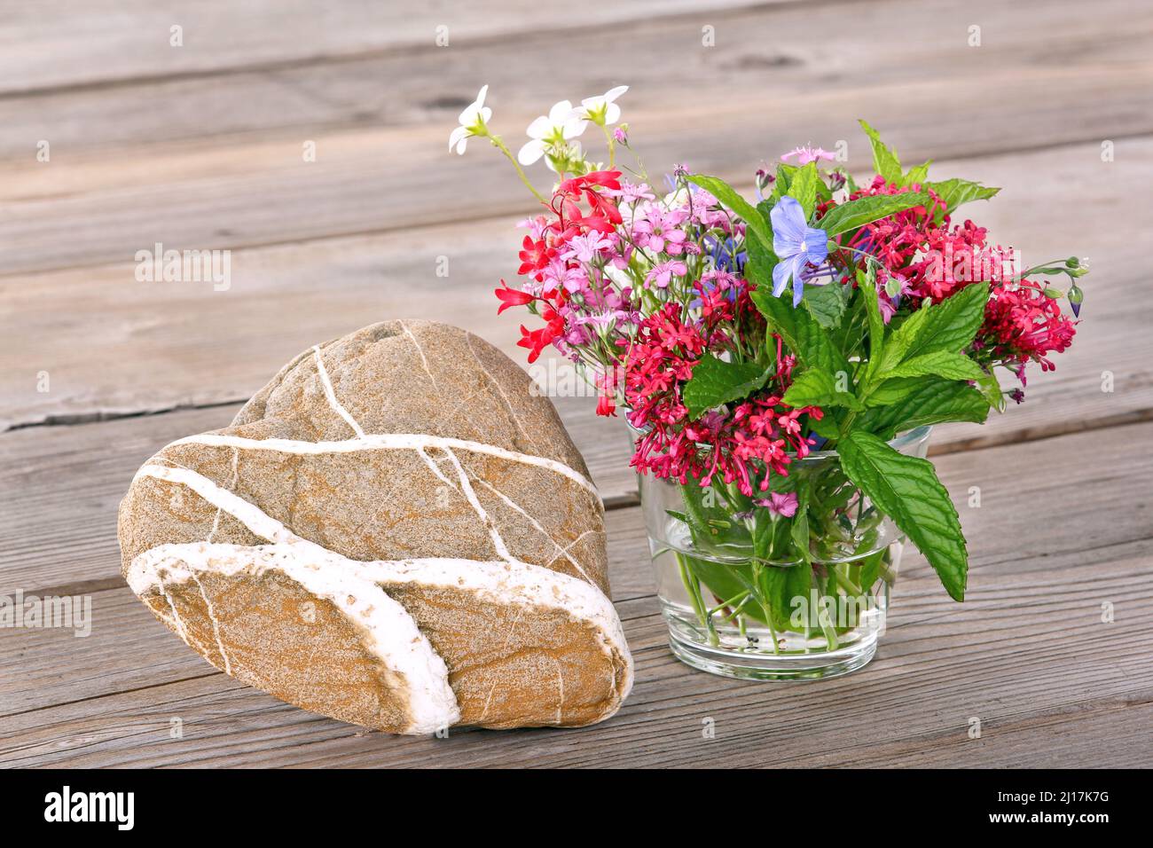 Heart-shaped stone with a small bouquet of flowers Stock Photo