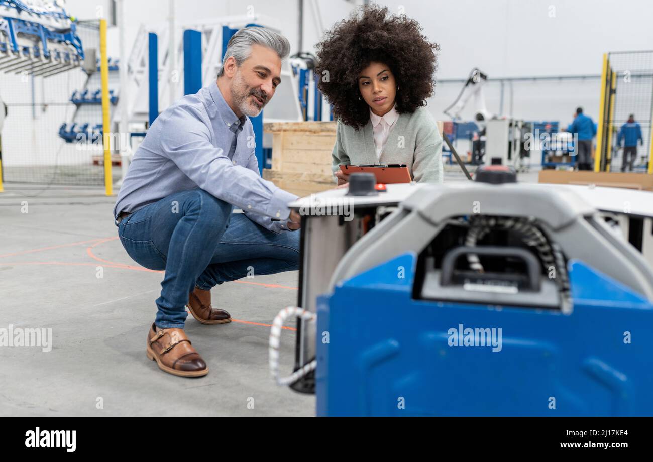 Engineer in squatting position discussing with developer in factory Stock Photo