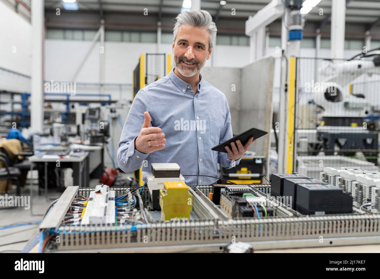 Smiling engineer holding tablet PC standing by machine in factory Stock Photo