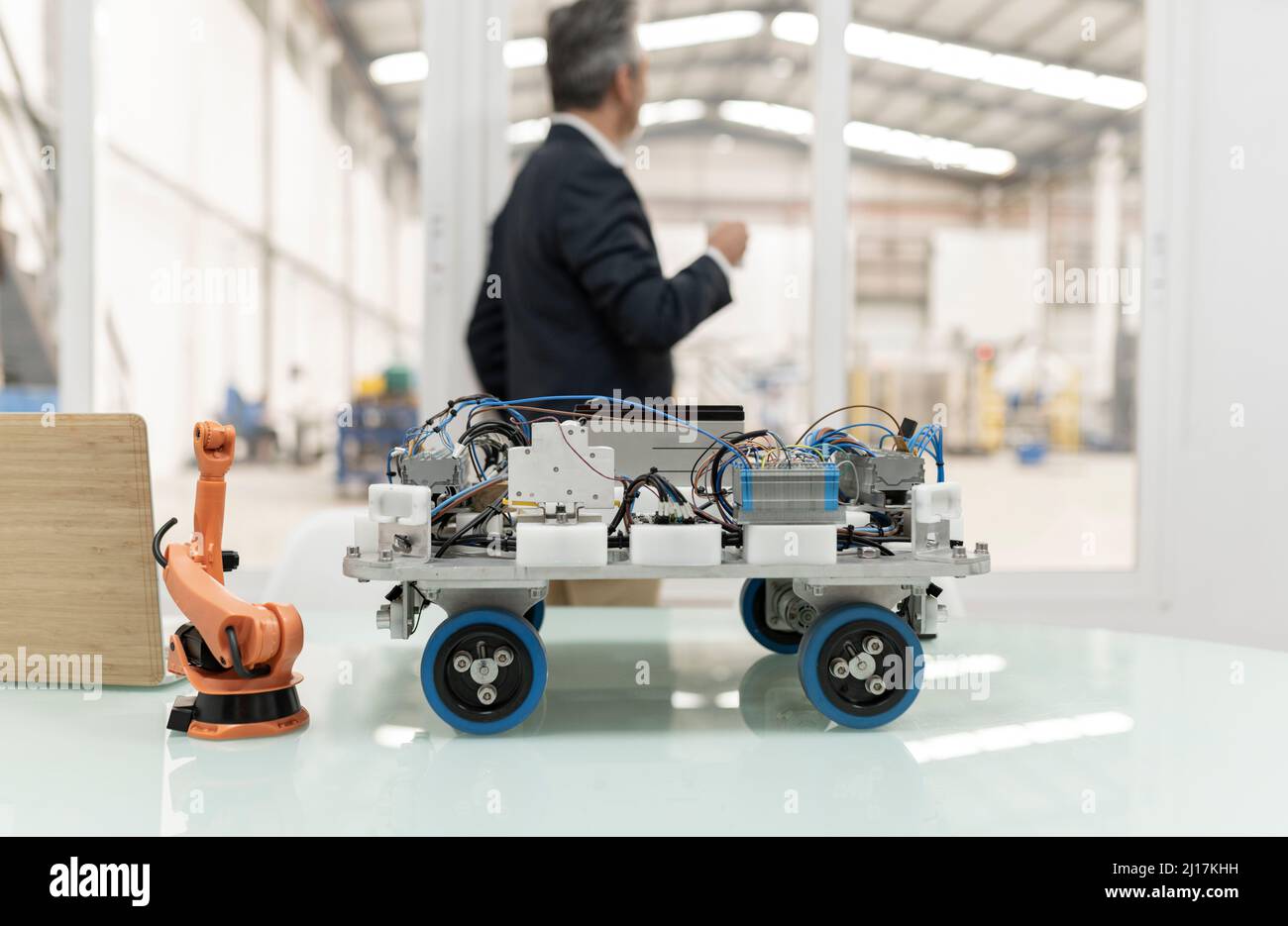 Model of robotic arm and vehicle on desk with businessman standing in background at factory Stock Photo