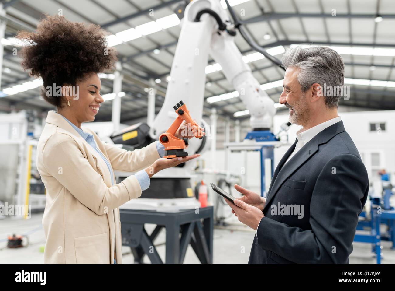 Smiling developer showing model of robotic arm to businessman in ...