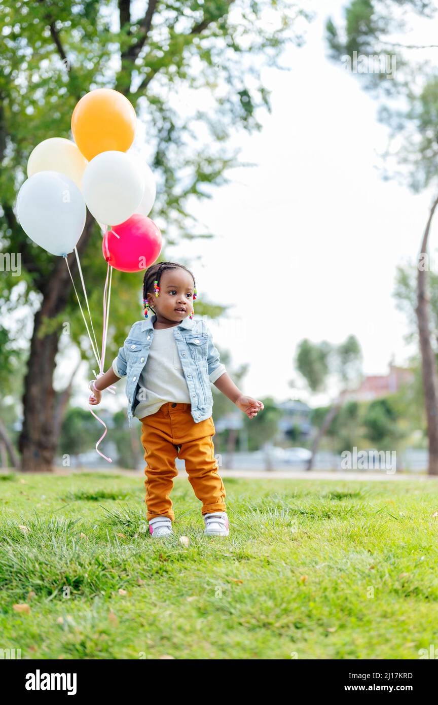 Cute little girl with balloons standing at park Stock Photo - Alamy