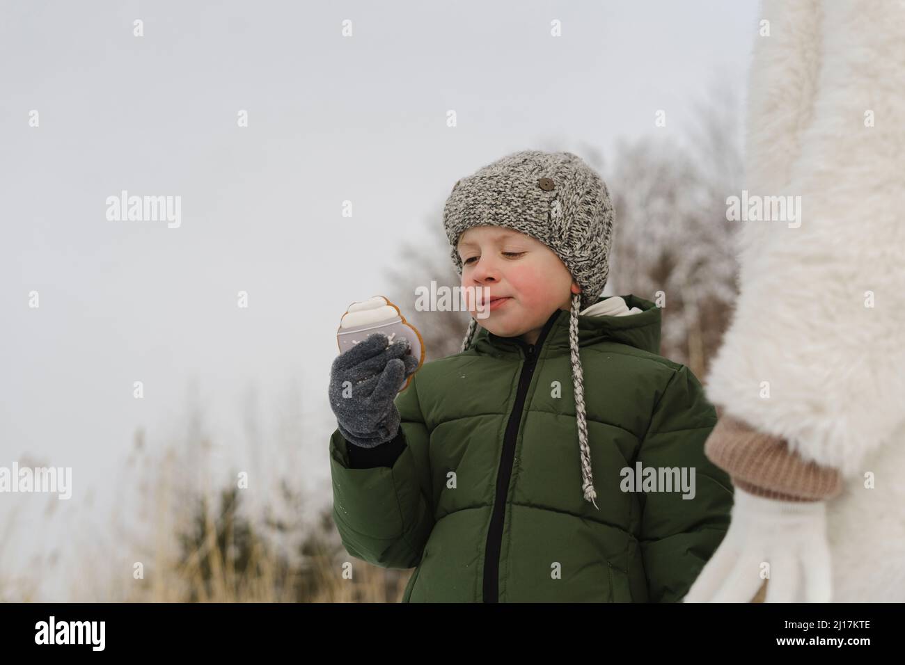Boy wearing knit hat eating cookie standing by mother in winter Stock Photo
