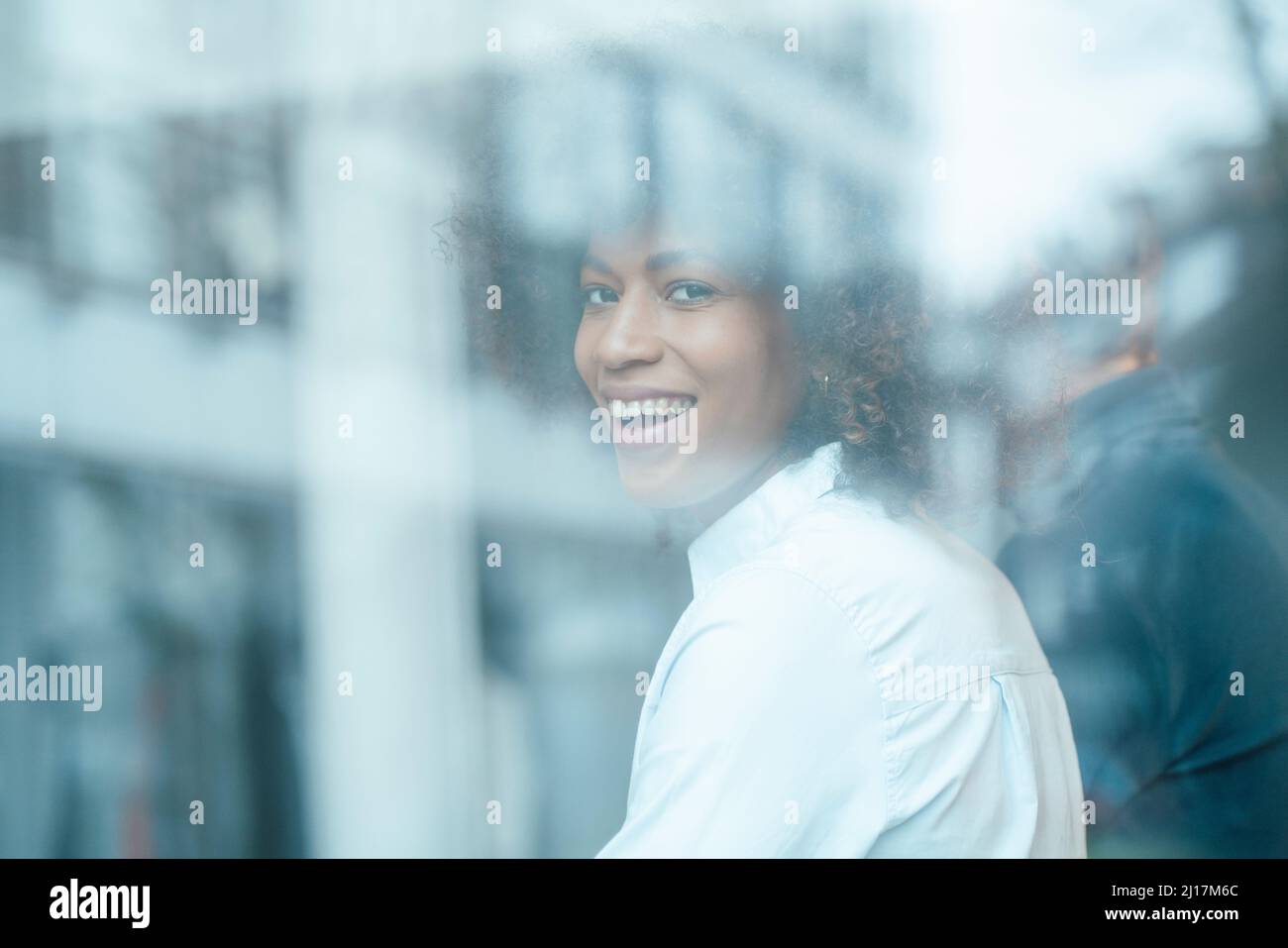 Happy businesswoman seen through glass of work place Stock Photo
