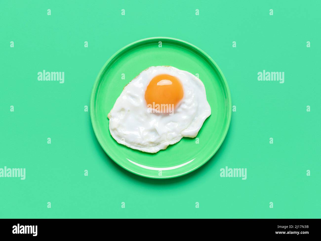 Single fried egg in a plate minimalist on a green table. Top view with a fried egg isolated on a colorful background. Stock Photo