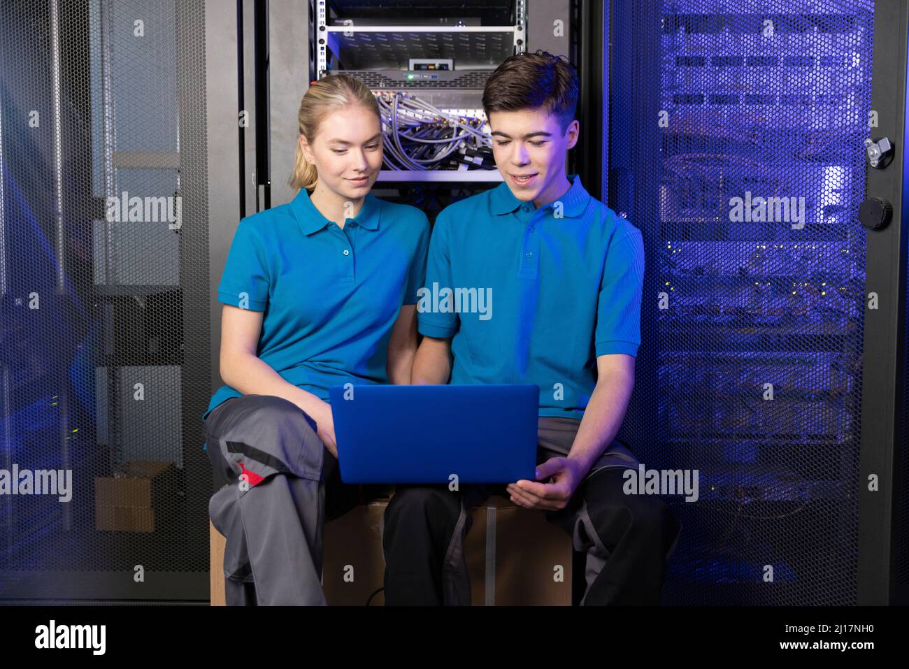 Technicians using laptop sitting in server room at industry Stock Photo