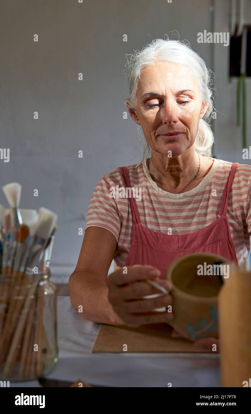 Woman holding clay pot sitting at table Stock Photo
