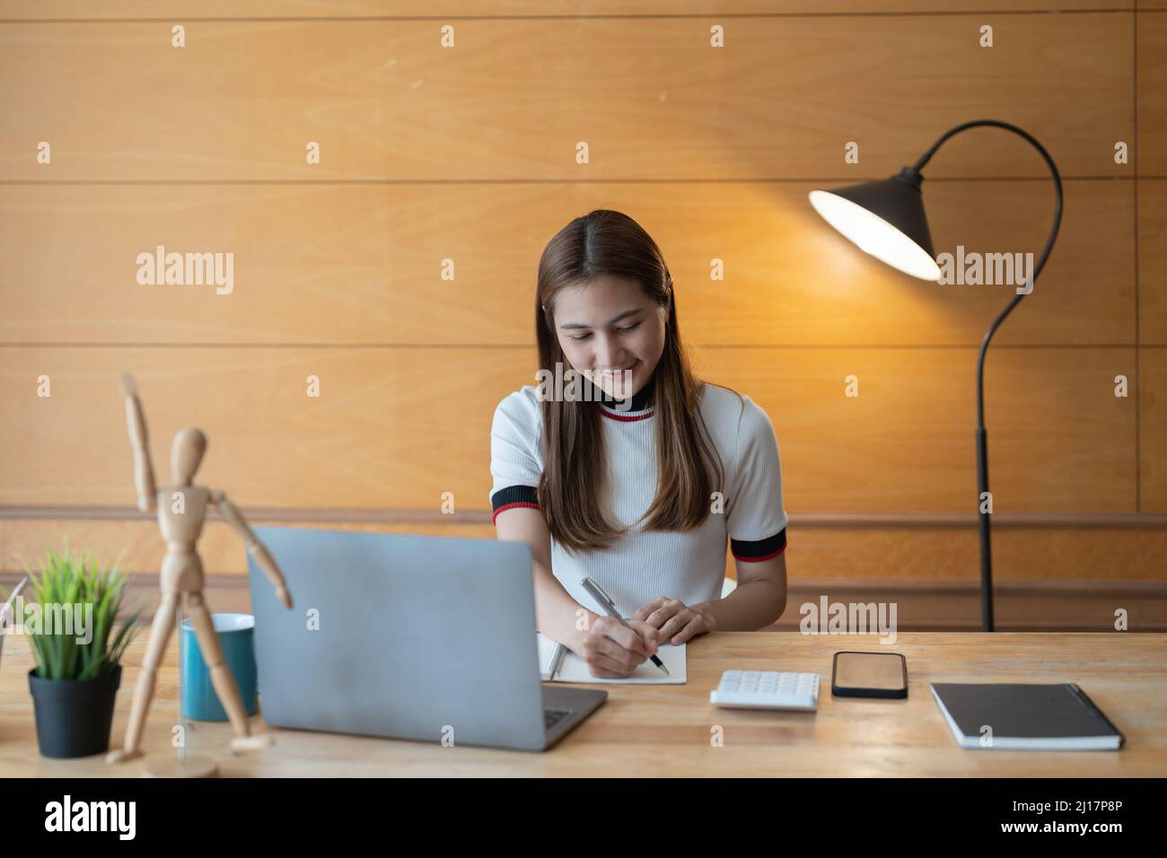 Young asian accountant taking note on notepad and using a laptop computer, calculator for financial. Stock Photo