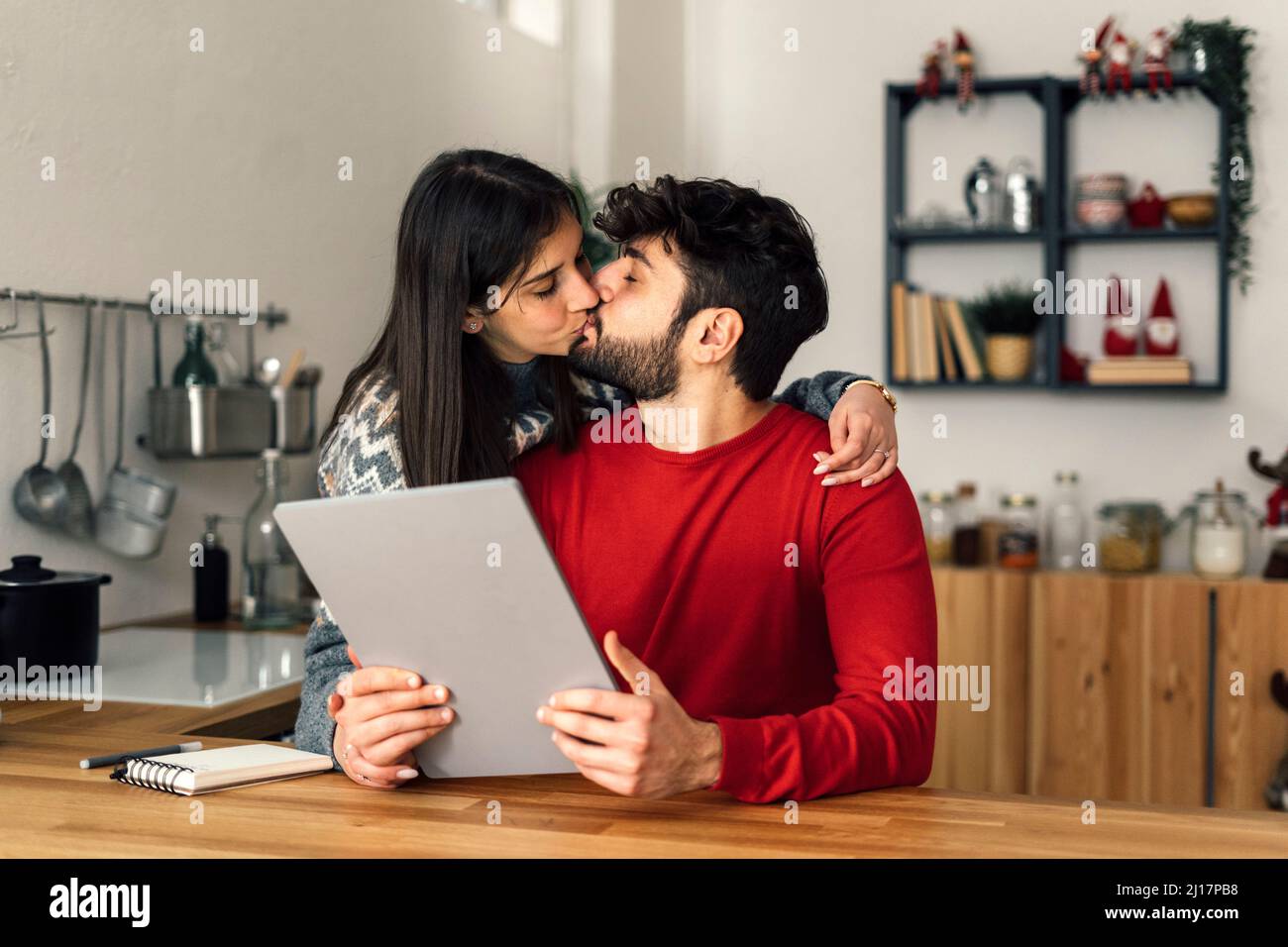 Man holding tablet PC kissing girlfriend in kitchen at home Stock Photo