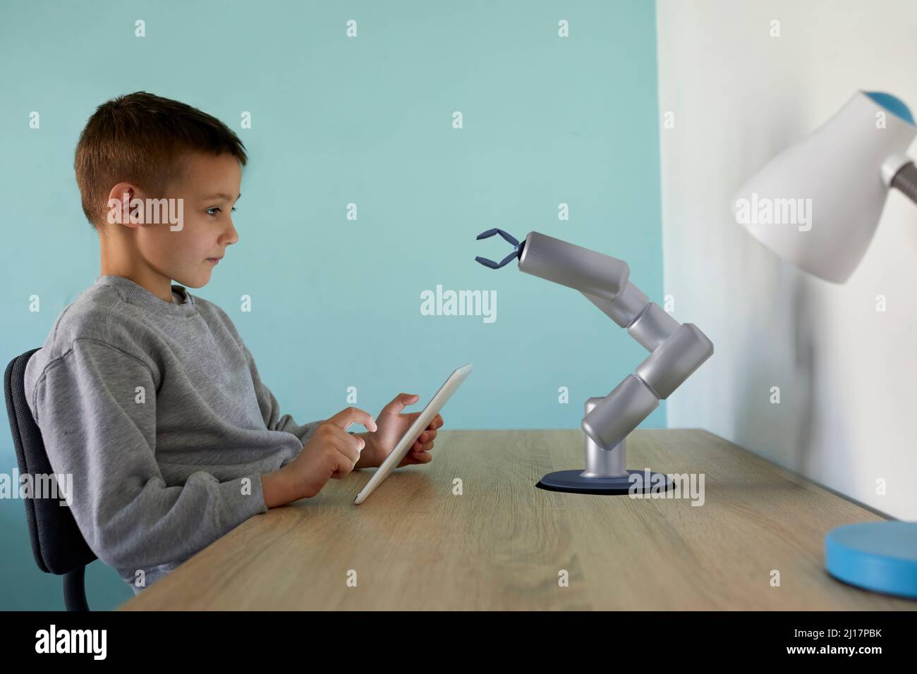 Boy controlling robotic arm through tablet PC sitting at table Stock Photo