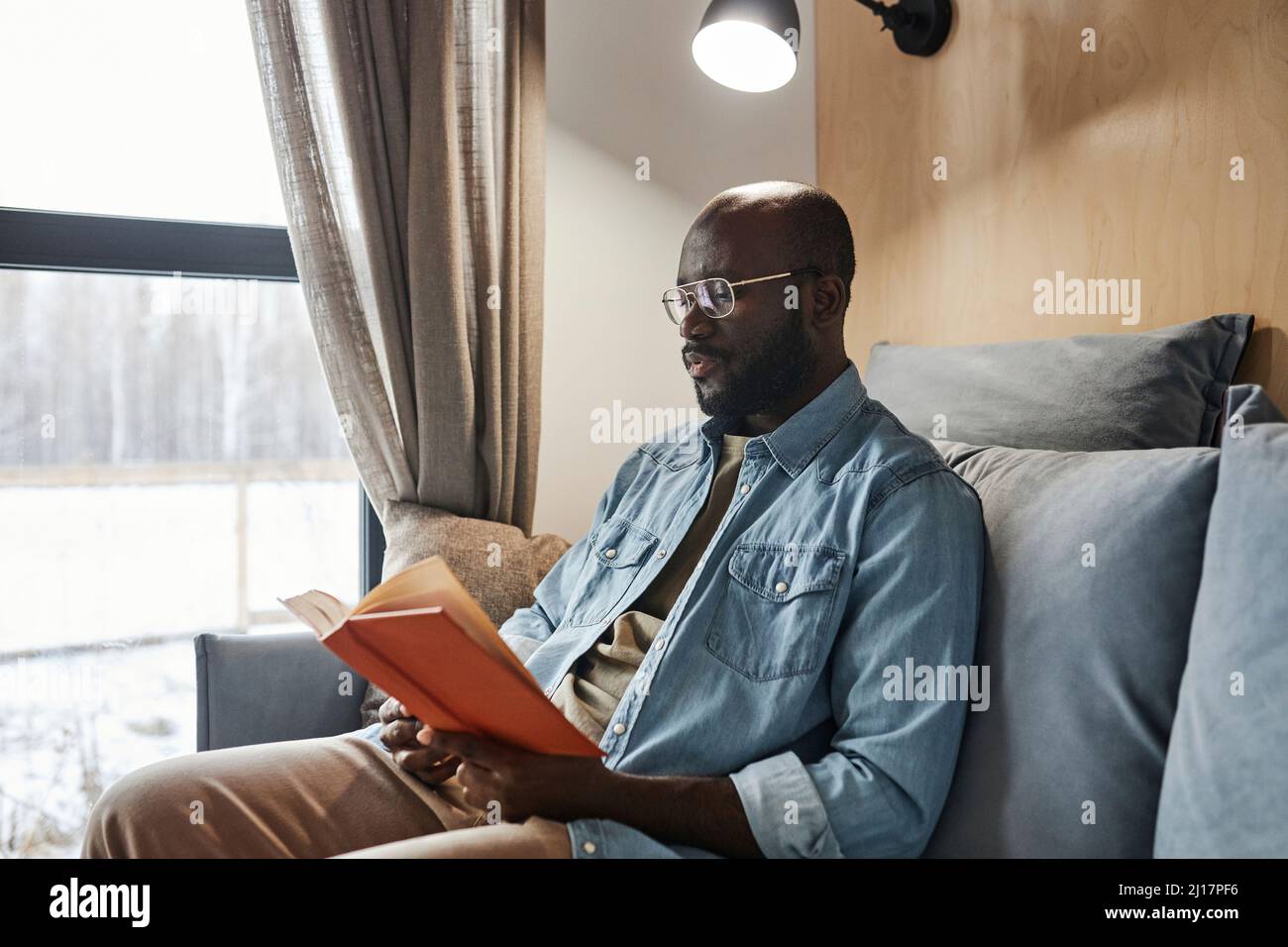 Young man reading novel on sofa at home Stock Photo